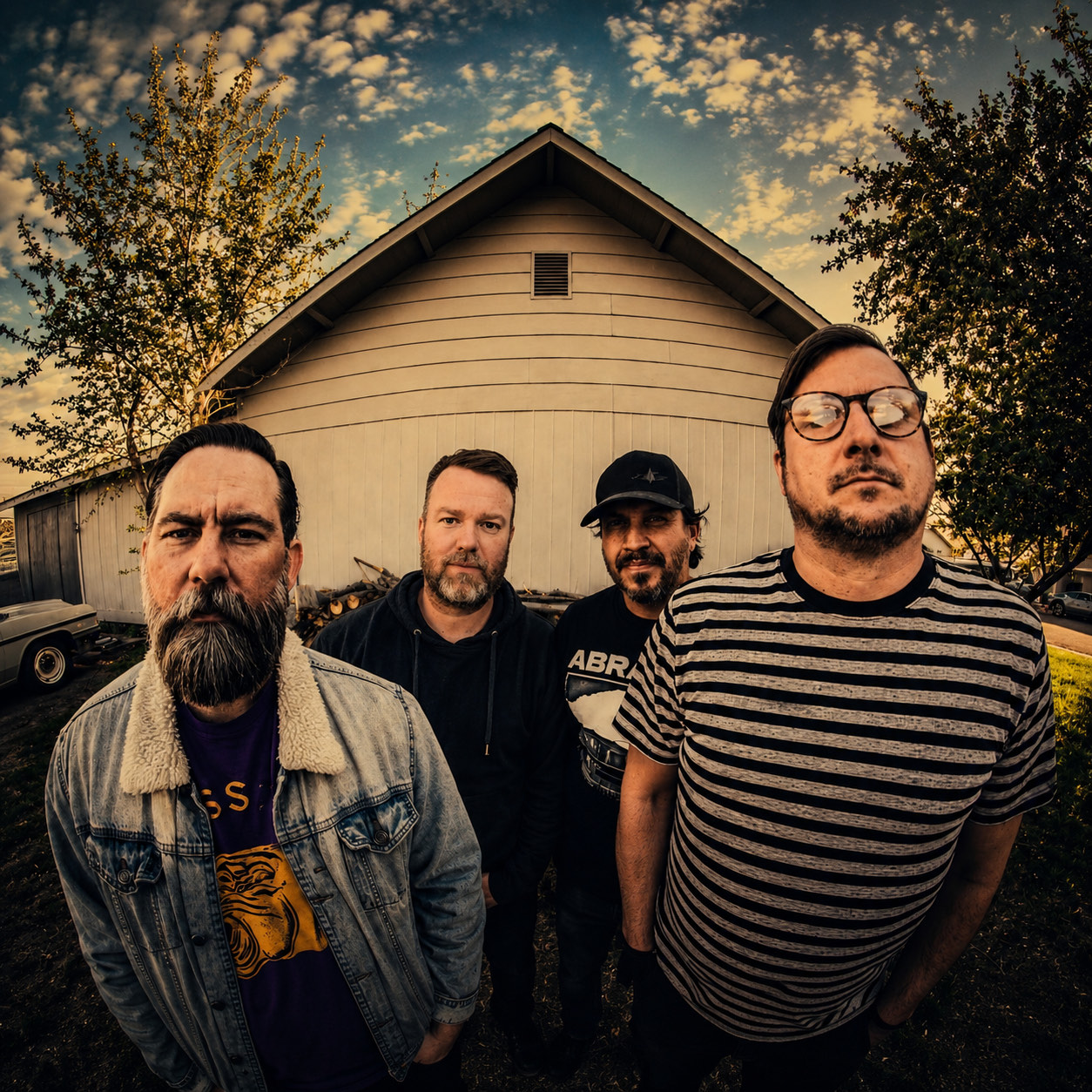 The four members of Yeah Nah Yeah standing in front of a white barn at sunset